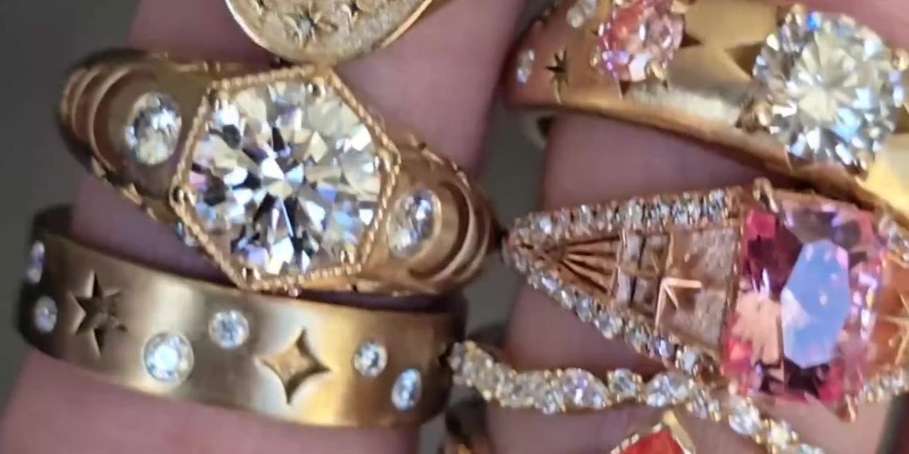 Hands wearing gold rings with cut gemstones in the light.
